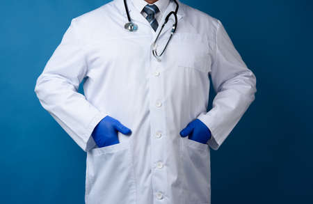 doctor in a white coat stands on a blue background, man in a tie and a stethoscope hangs around his neckの写真素材