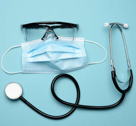 disposable medical mask, plastic goggles and stethoscope on blue background, top viewの写真素材