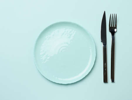 round ceramic plates, fork with knife on a green background, top view. Table settingの写真素材