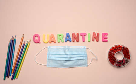 disposable medical mask and the inscription quarantine from plastic multicolored letters on a beige background, top view The concept of closing educational institutions during epidemics and pandemicの写真素材
