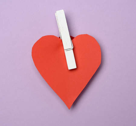 red paper heart pinned on a wooden clothespin, purple backgroundの写真素材