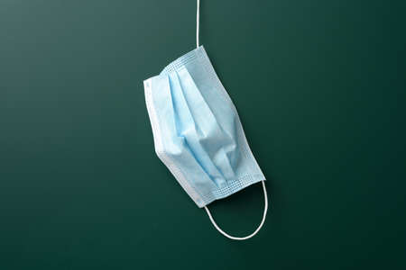 disposable medical mask hanging on blank green chalk board background, quarantine concept