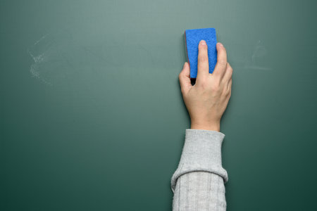 woman's hand wipes a green chalk board with a blue sponge, close upの写真素材