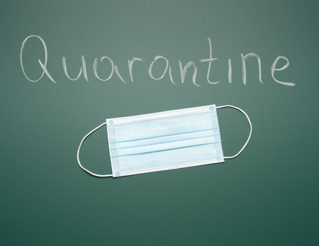 inscription quarantine on a green chalk board and disposable medical mask, the closure of educational institutions during a pandemicの写真素材