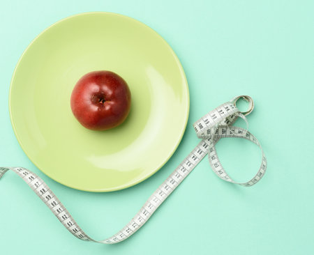 red ripe apple lies in a green round plate next to a measuring tape, weight loss conceptの写真素材