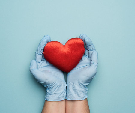 two hands in blue latex gloves holding a red textile heart, donation concept, close upの写真素材