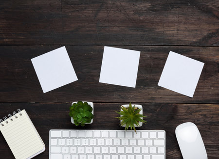 white wireless keyboard and mouse on a wooden brown table, next to three blank white sheets of paper, top view, copy spaceの写真素材