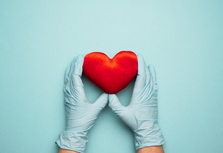 two hands in blue latex gloves holding a red textile heart, donation concept, close upの写真素材
