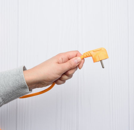 female hand holds orange cable with plug for socket, white backgroundの写真素材