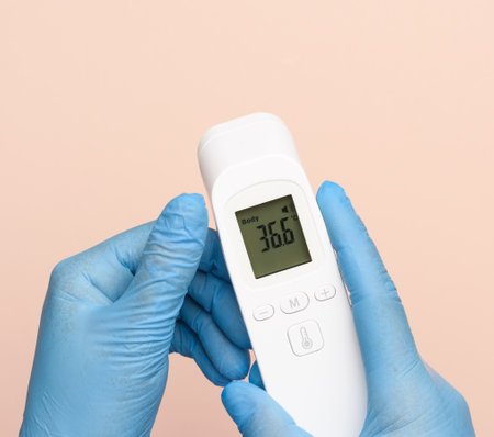 hand in blue latex gloves hold an electronic thermometer to measure temperature, non-contact device,...