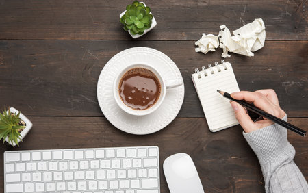 white wireless keyboard and mouse on a wooden brown table, next to a white cup with coffee, top viewの写真素材