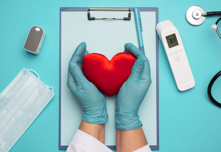 two hands in blue latex gloves holding a red textile heart, donation concept, close upの写真素材