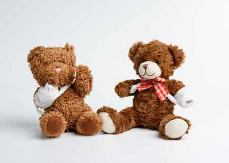 brown curly teddy bear with rewound paw with white gauze bandage on white background, concept of injuries in children or animalsの写真素材