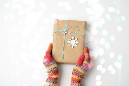 hands in knitted mittens hold a box in brown paper and tied with a rope on a white background with bokeh, top viewの写真素材