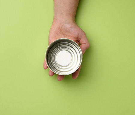 open metal round tin can in a female hand on a green background, top view