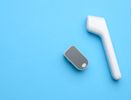 plastic white electronic non-contact thermometer and blood oxygen meter, blue backgroundの写真素材