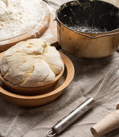 kneaded dough made of white wheat flour in a wooden plate and a metal kneading bucket, close upの写真素材