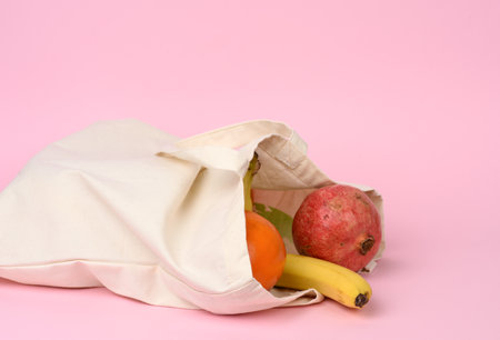 beige textile bag with fresh fruits on a pink background, zero waste