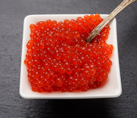 red chum salmon caviar in a white ceramic bowl on a black slate stone background, close upの写真素材