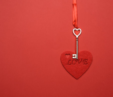 metal key and red felt heart hang on red ribbon, red backgroundの写真素材