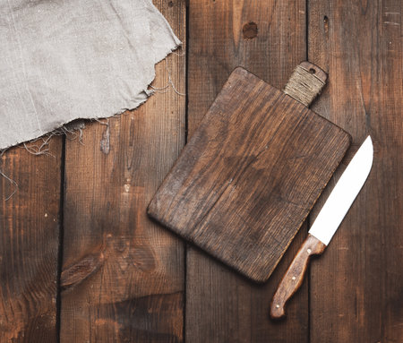 knife and old brown rectangular wooden kitchen cutting board and gray linen napkin on the table, top viewの写真素材