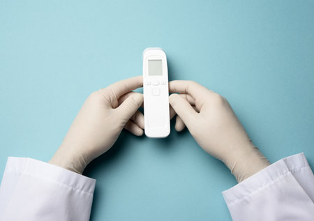 hand in white latex gloves hold an electronic thermometer to measure temperature, non-contact deviceの写真素材