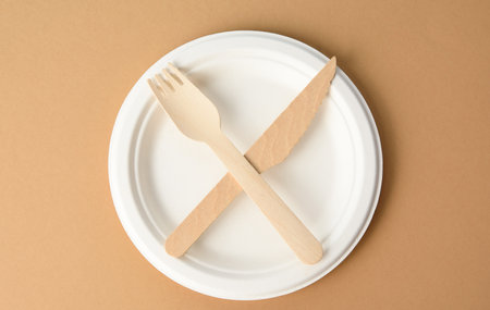 empty white paper plate and wooden knife and fork, objects crossed
