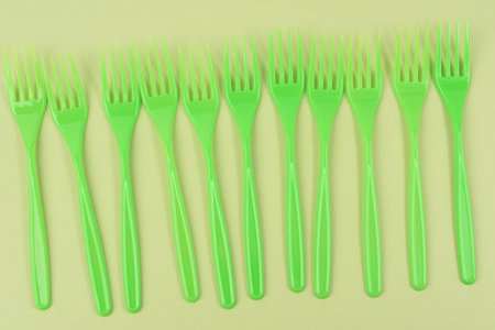 stack of green plastic forks on a green background, top view