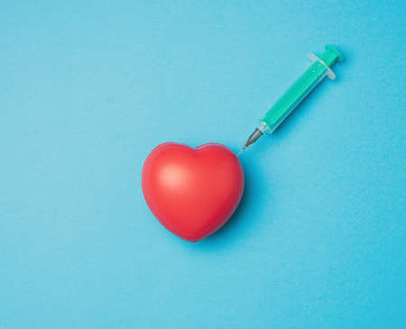 red heart and stuck needle of a plastic syringe inside of it on a blue background, top viewの写真素材