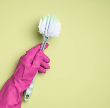 female hand in purple rubber gloves holds a plastic cleaning brush on green backgroundの写真素材
