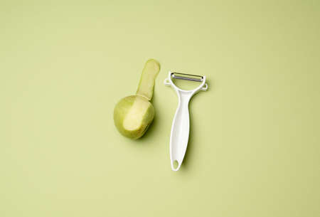 plastic knife for peeling vegetables and fruits and a green apple on a green background, top viewの写真素材
