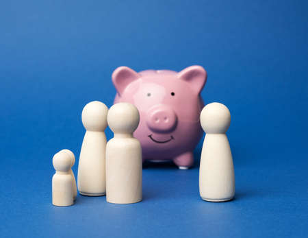wooden family figurines on pink ceramic piggy bank background on blue background, saving conceptの写真素材