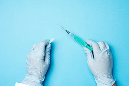 two hands in blue latex gloves hold a plastic syringe on a blue background, close up