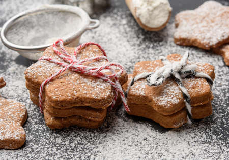 Star shaped baked gingerbread cookies sprinkled with powdered sugar on a black table, close up