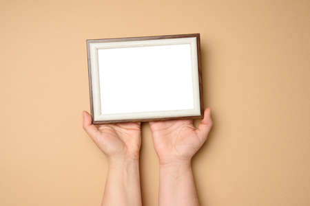 two female hands holding a empty rectangular blank wooden frame, beige backgroundの写真素材
