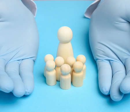 family of wooden figures and two hands in blue latex gloves, protection and patronage, insurance, top viewの写真素材