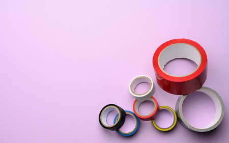 various skeins of multicolored scotch tape and electrical tape on a purple background, copy space