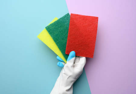female hand in a white rubber glove holds multi-colored kitchen sponges on a purple background, close upの写真素材