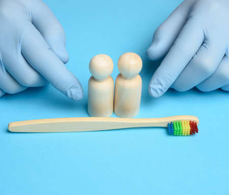 wooden figurines and hands of a doctor in medical blue gloves, next to a wooden toothbrushの写真素材