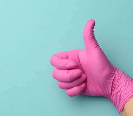 hand in pink medical glove shows right-handed gesture like on a blue background, concept of...