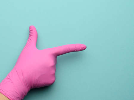 female hand in a pink latex glove on a blue background, forefinger raised, close upの写真素材