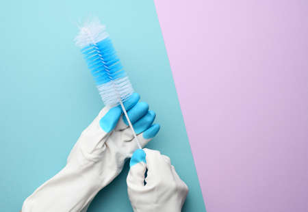 female hand in white rubber gloves holds a plastic cleaning brush on a blue background, copy space