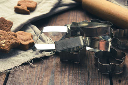 metal cookie cutters and wooden rolling pin on a wooden background, close up