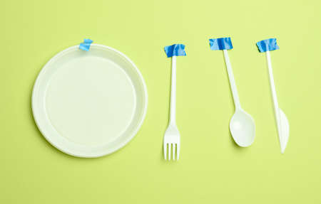 disposable plastic forks and spoons glued with blue tape on a green background, avoiding plastic, preserving the environmentの写真素材