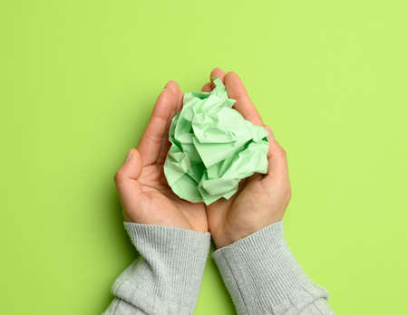 mint green sheet of paper in a female hand on a green background, top viewの写真素材