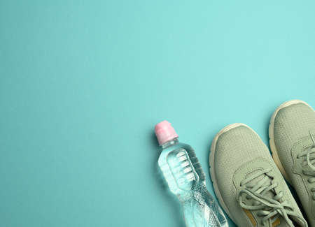pair of sports sneakers and a bottle with mineral water on a blue background, top view, copy spaceの写真素材