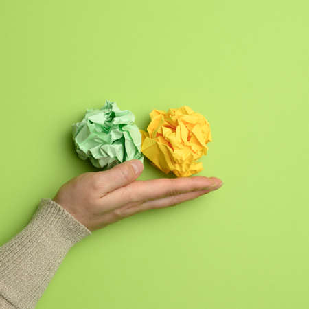 green and yellow crumpled ball of paper in a female hand on a green background