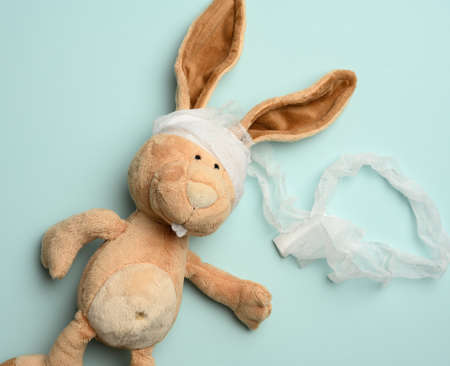 plush beige rabbit with a bandaged head with a white medical bandage on a blue background, top viewの写真素材