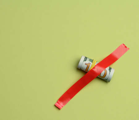 rolled paper american hundred dollar bills glued with red tape on a green background, close up
