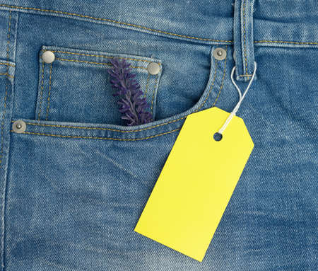 blank rectangular cardboard yellow tag on blue jeans background, close upの写真素材